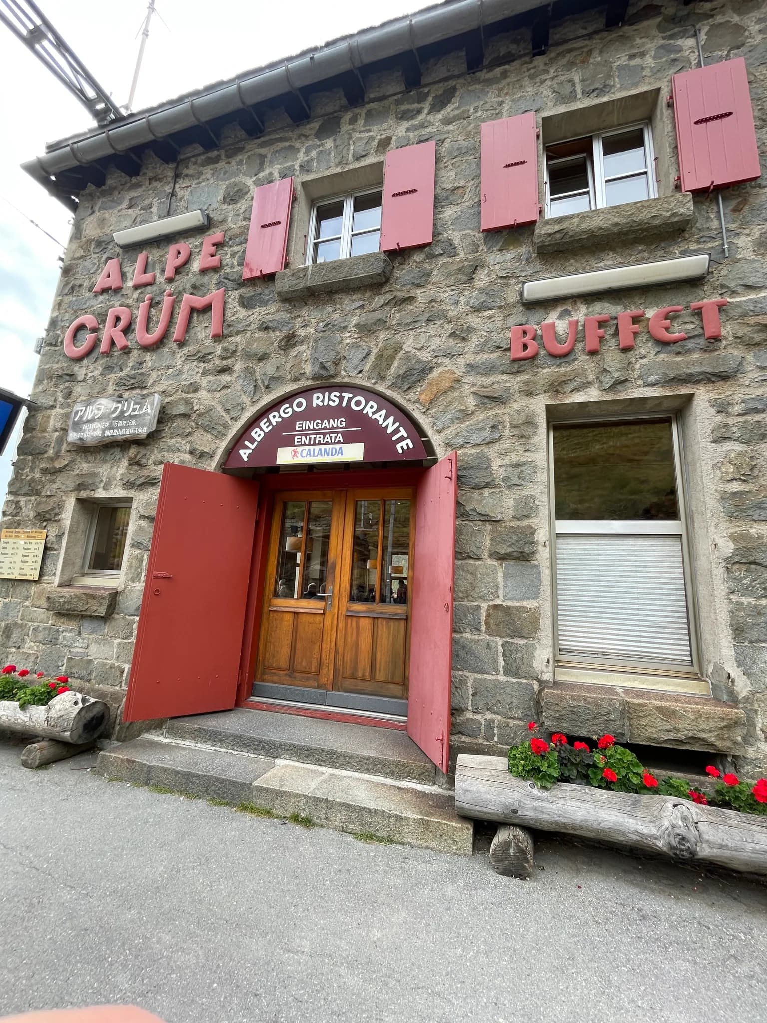 Stone exterior of Alp Grüm station and restaurant with red shutters and entrance signs