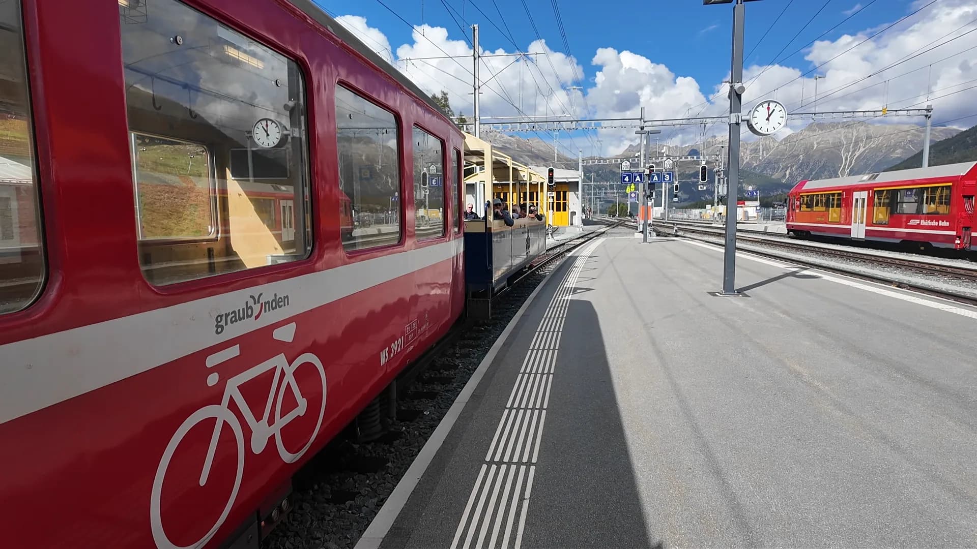 Yellow open-air Rhätische Bahn carriage attached to a regional train at Pontresina