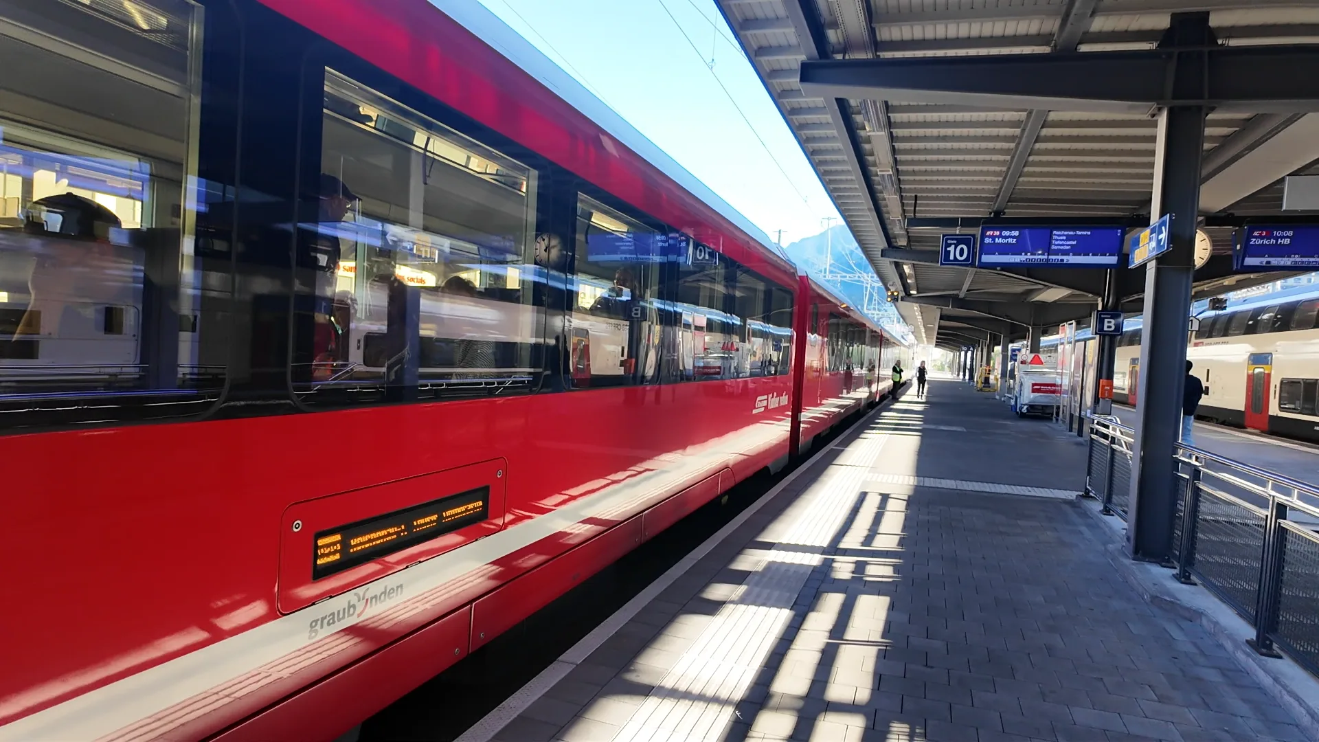 Rhätische Bahn regional train and Chur departure board showing IR38 to St. Moritz at 09:58