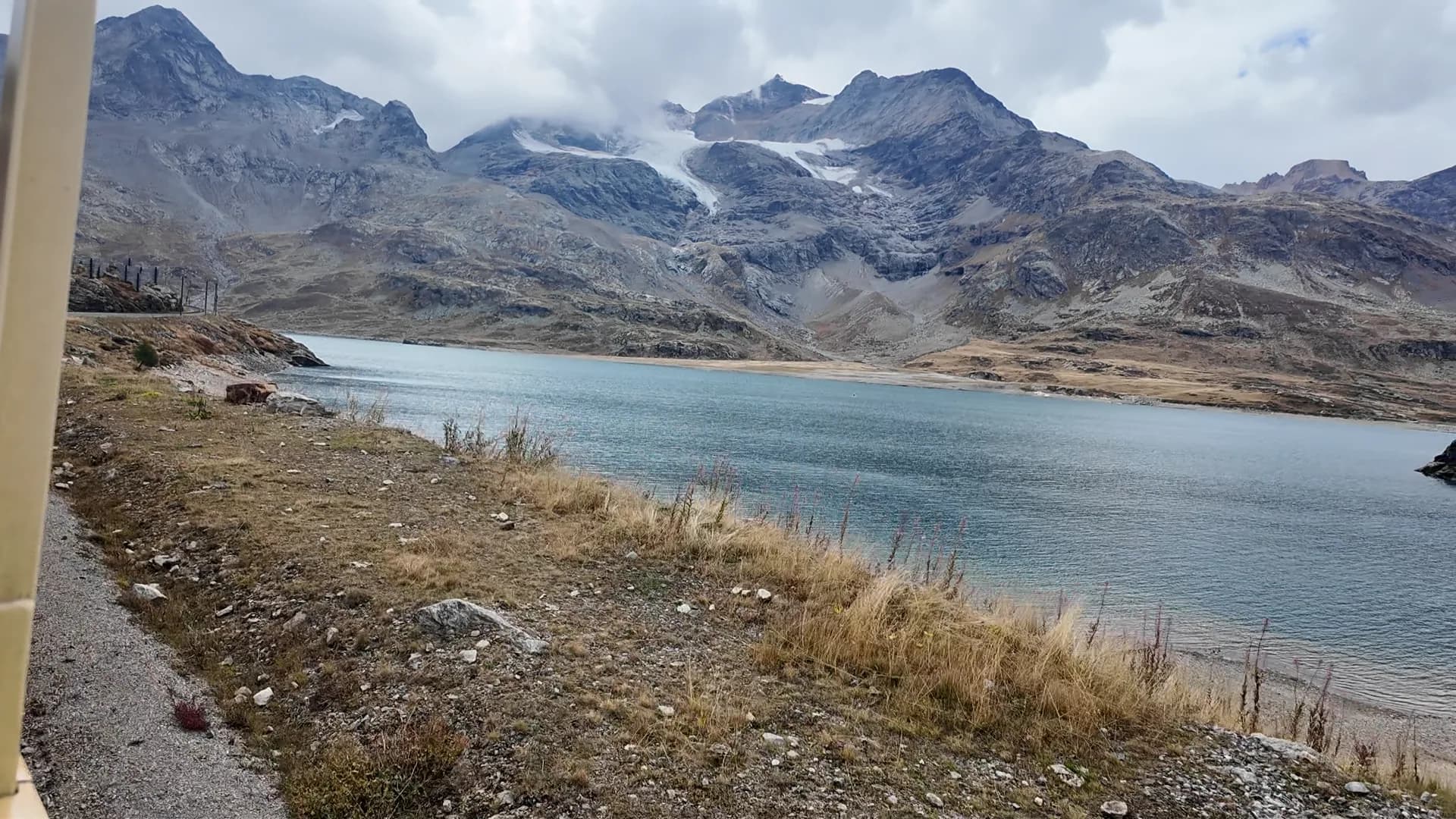 Pale blue Lago Bianco and rocky mountains seen from the regional train near the Bernina Pass