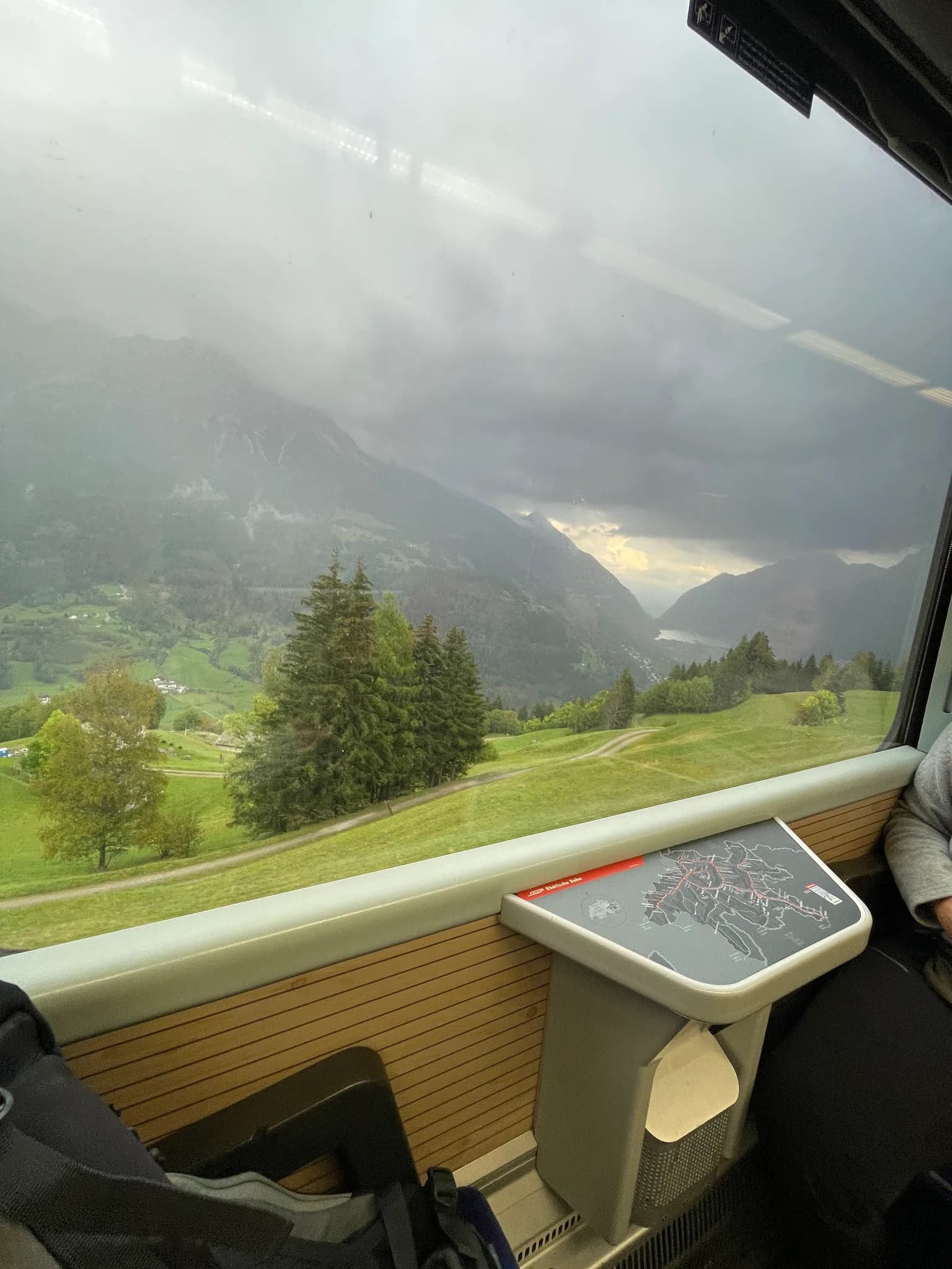Rainy green valley seen through the regional train window during the descent from Alp Grüm