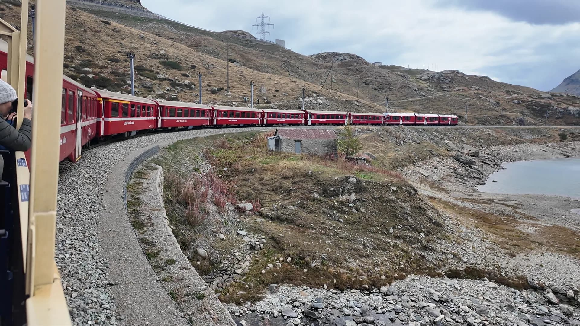Long red Rhätische Bahn train curving through the mountains beside a high Alpine lake